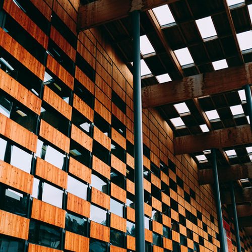 A low angle view of a modern building with wooden walls and blue windows under white lamp lights